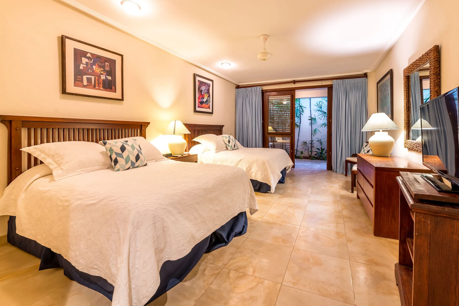Un dormitorio con dos camas, lámparas de noche y cortinas junto a las puertas del balcón.