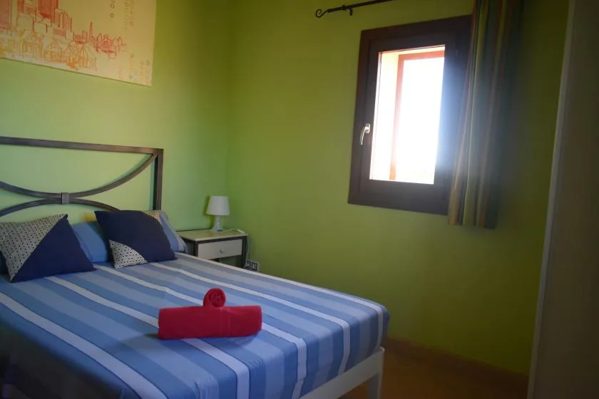 Un dormitorio con una cama a rayas y una ventana en la pared verde.
