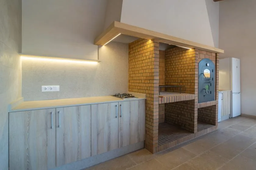 Una cocina con gabinetes claros, una placa de cocción y una zona de barbacoa de ladrillo.