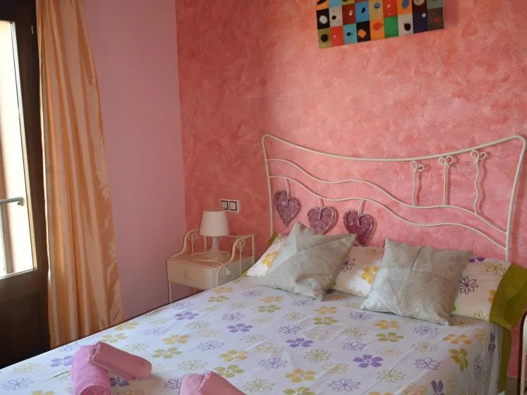 Un dormitorio con una cama cubierta de ropa de cama floral y una pared rosa.