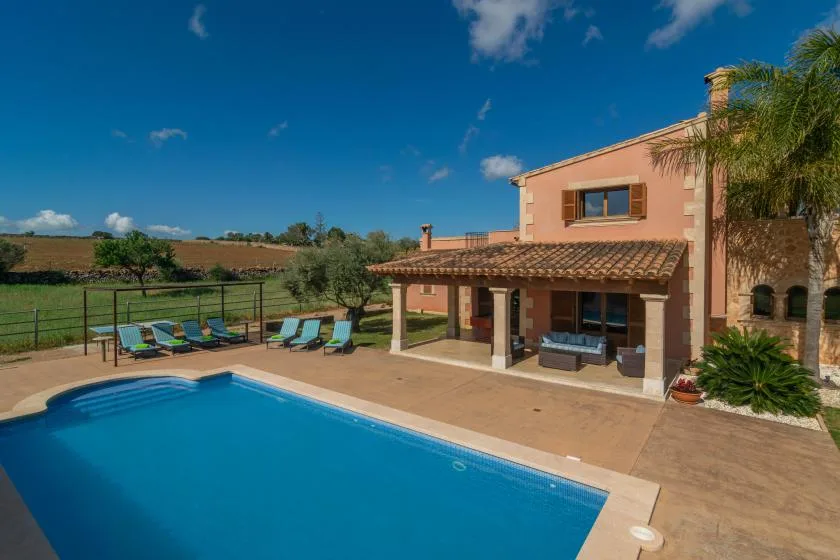 Una piscina junto a una casa de dos plantas con un patio cubierto.