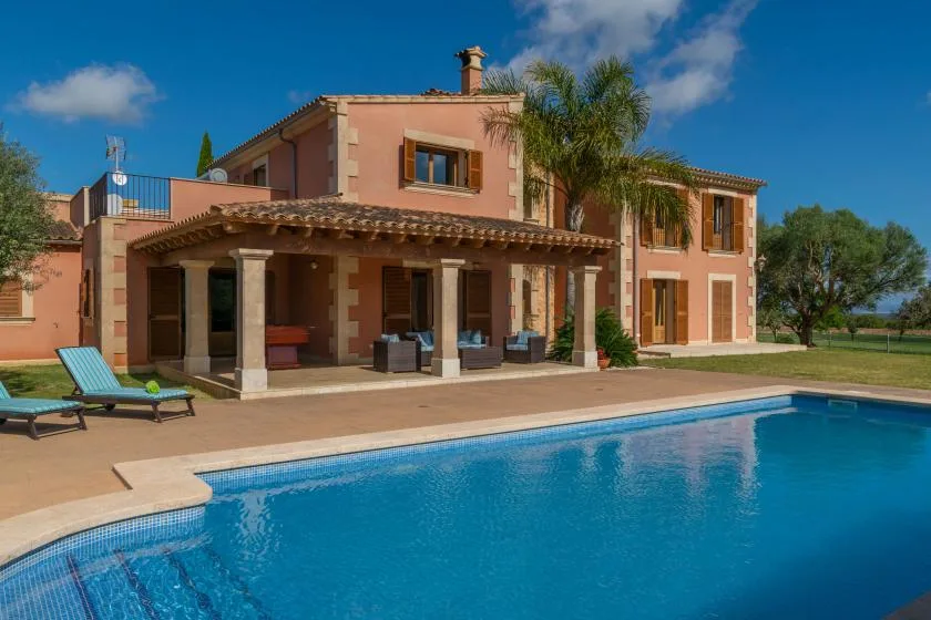 Una casa de color melocotón está junto a una piscina, con asientos en un patio cubierto.