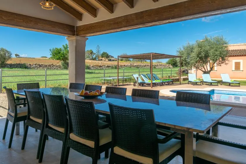 Un comedor exterior cubierto da a una piscina y tumbonas.