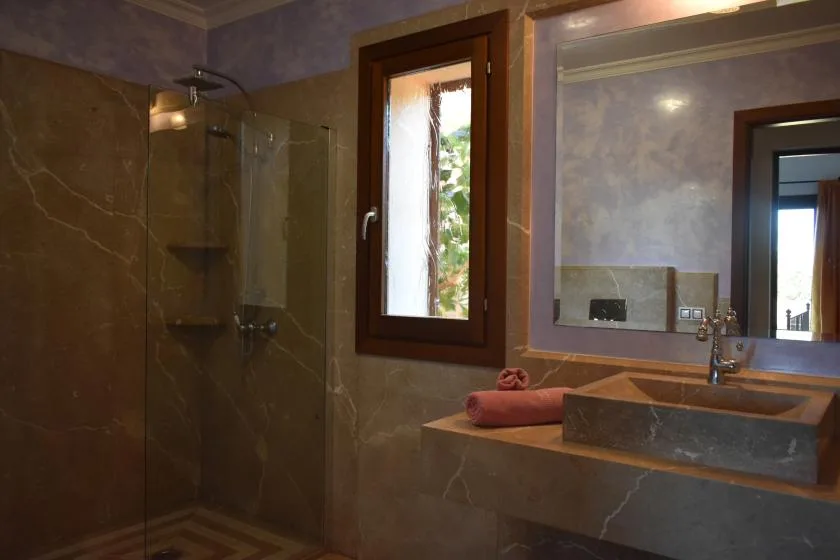 Un baño con ducha de vidrio, lavabo de piedra y una ventana.