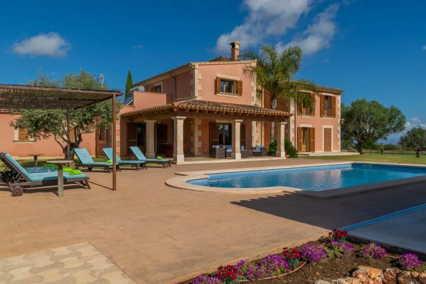 Una casa de color terracota da a una piscina y un patio pavimentado.
