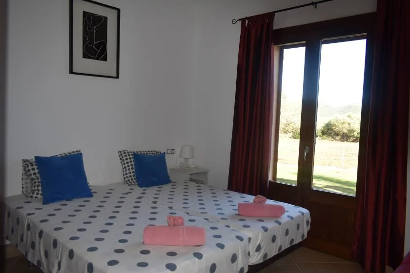Un dormitorio con una cama doble cubierta con ropa de cama blanca y azul con puntos, junto a una ventana.