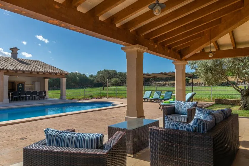 Una zona de estar al aire libre y cubierta da a una piscina y a un espacio abierto.
