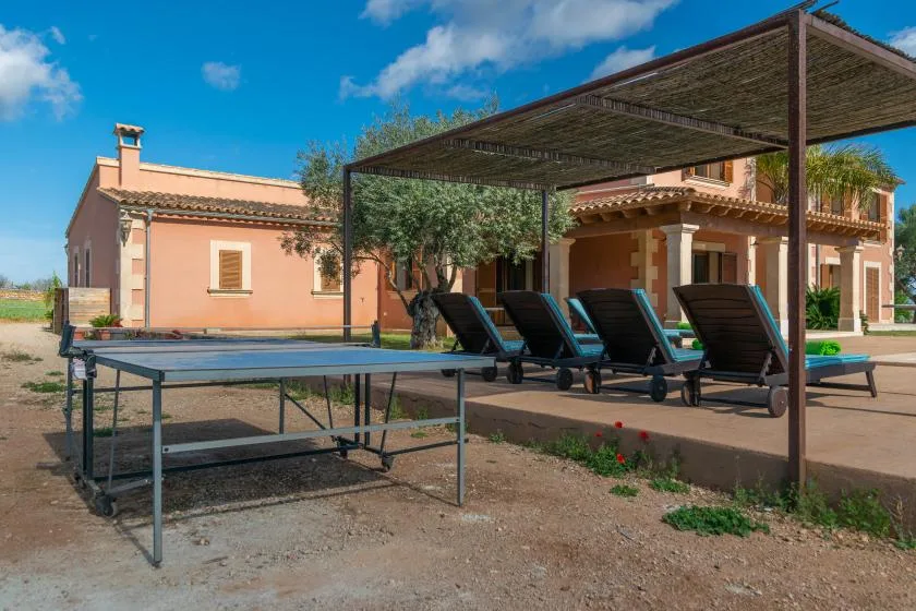 Un patio exterior con asientos bajo una pérgola sombreada junto a una casa.