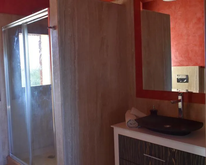 Un baño con una ducha de vidrio y un lavabo oscuro sobre un tocador.
