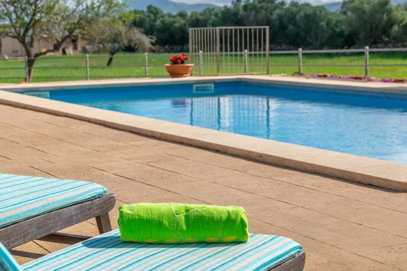 Una piscina al aire libre junto a una terraza pavimentada, con tumbonas a rayas en primer plano.