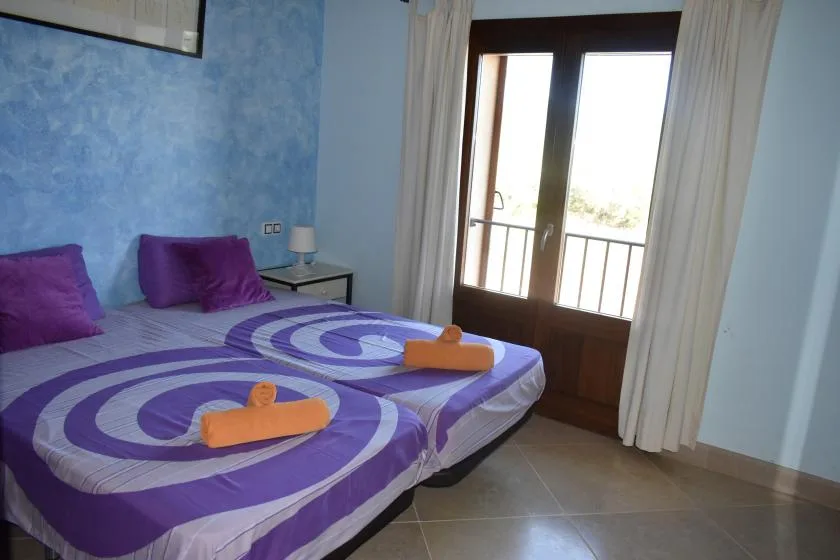 Un dormitorio con dos camas vestidas de morado junto a una puerta acristalada con cortinas.