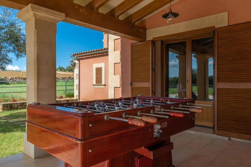 Una mesa de futbolín está en un patio cubierto junto a puertas de vidrio.