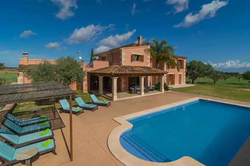Un patio de villa da a una piscina, con tumbonas junto al agua.