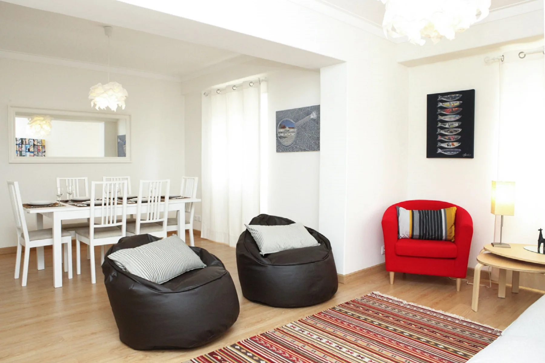 A bright living and dining area has beanbag seating, a dining table, and a red armchair.