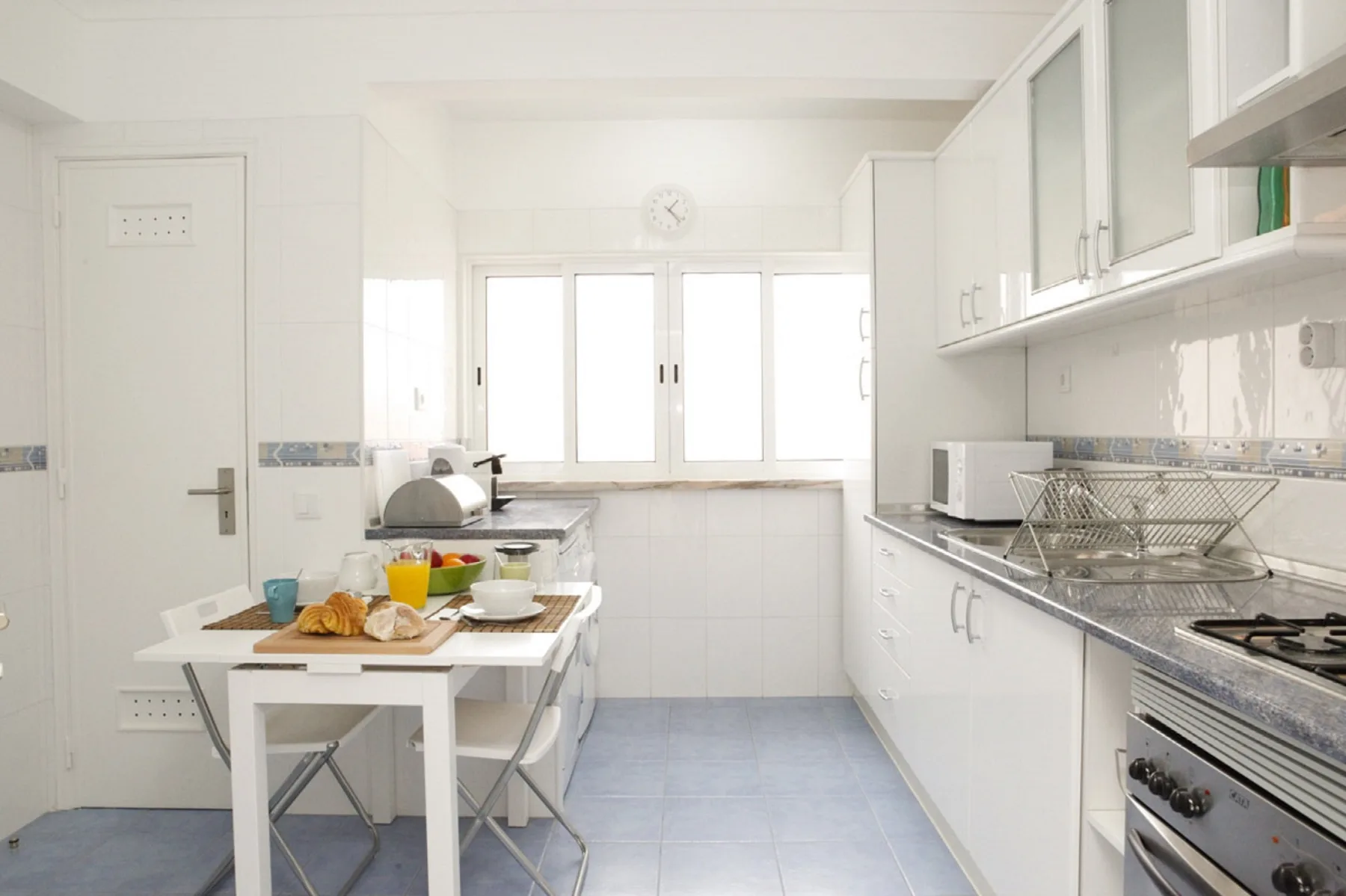 A bright kitchen with white cabinets, a dining table, and large windows.