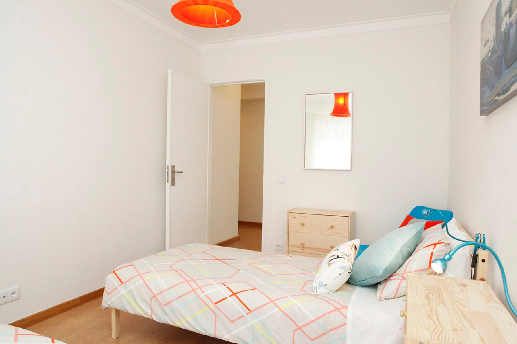 A bedroom with a bed, colorful bedding, and a small dresser.