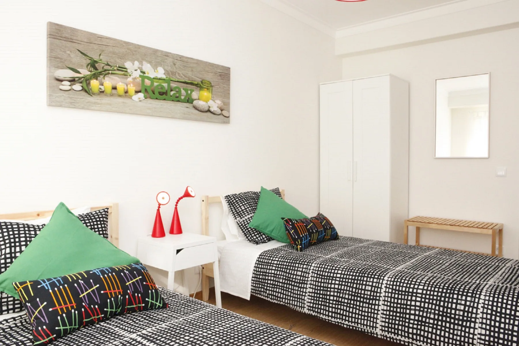 A bright bedroom with two beds, patterned bedding, and a small bedside table.