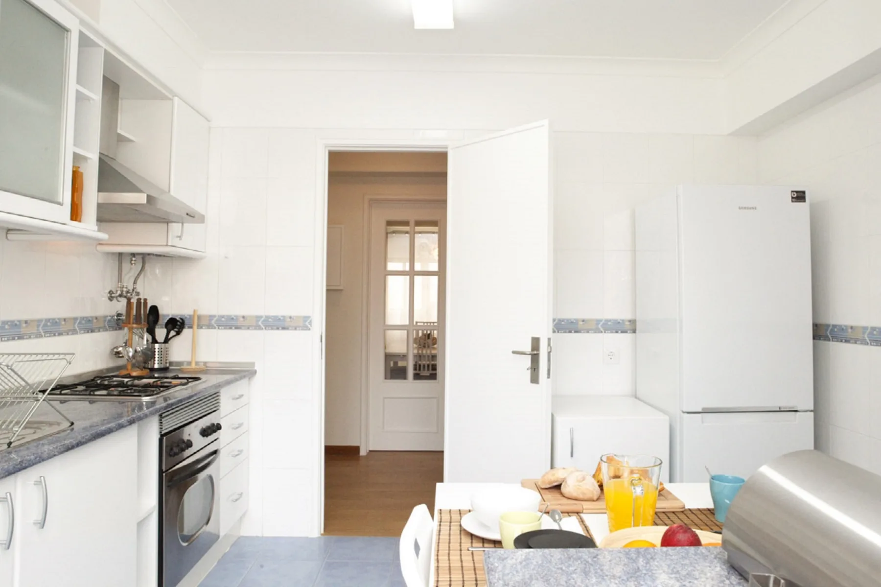 A bright kitchen with white cabinets, a refrigerator, and a dining table.