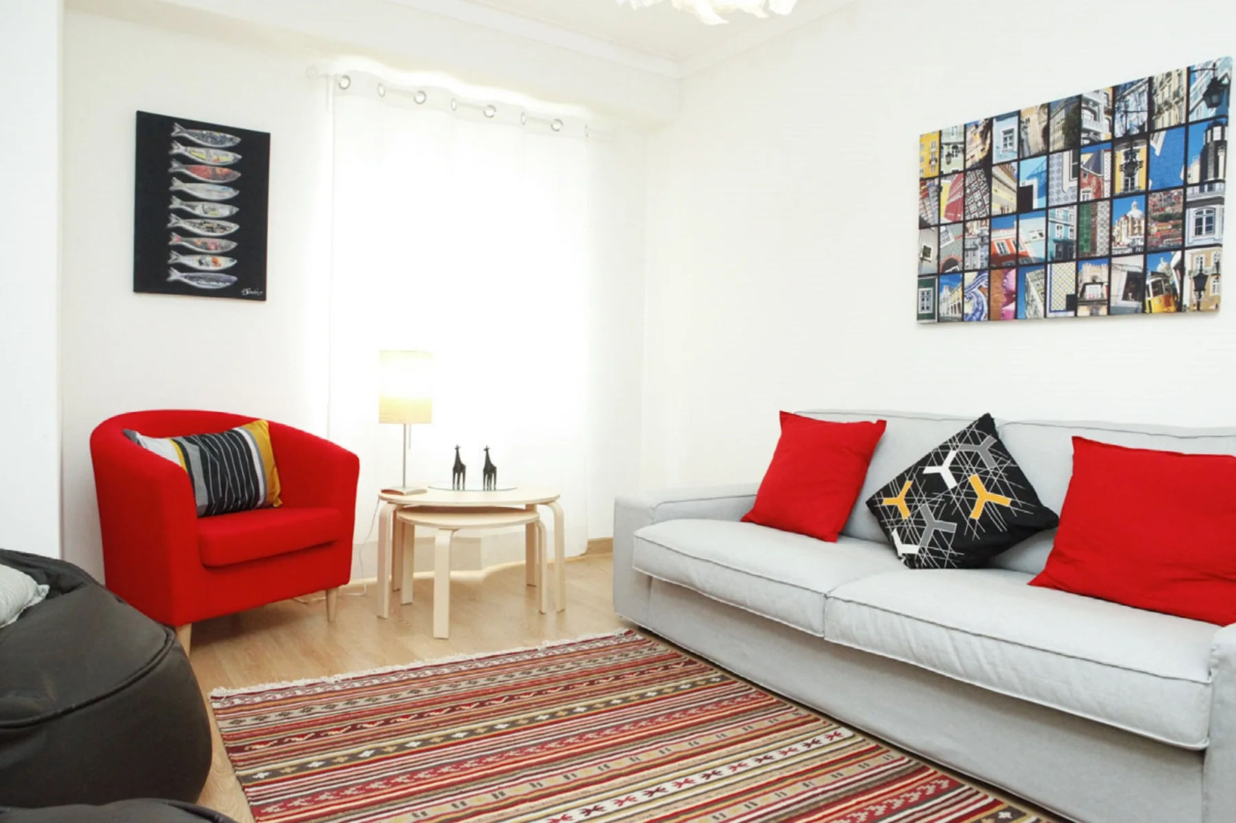 A bright living room has a white sofa, red armchair, and patterned rug.