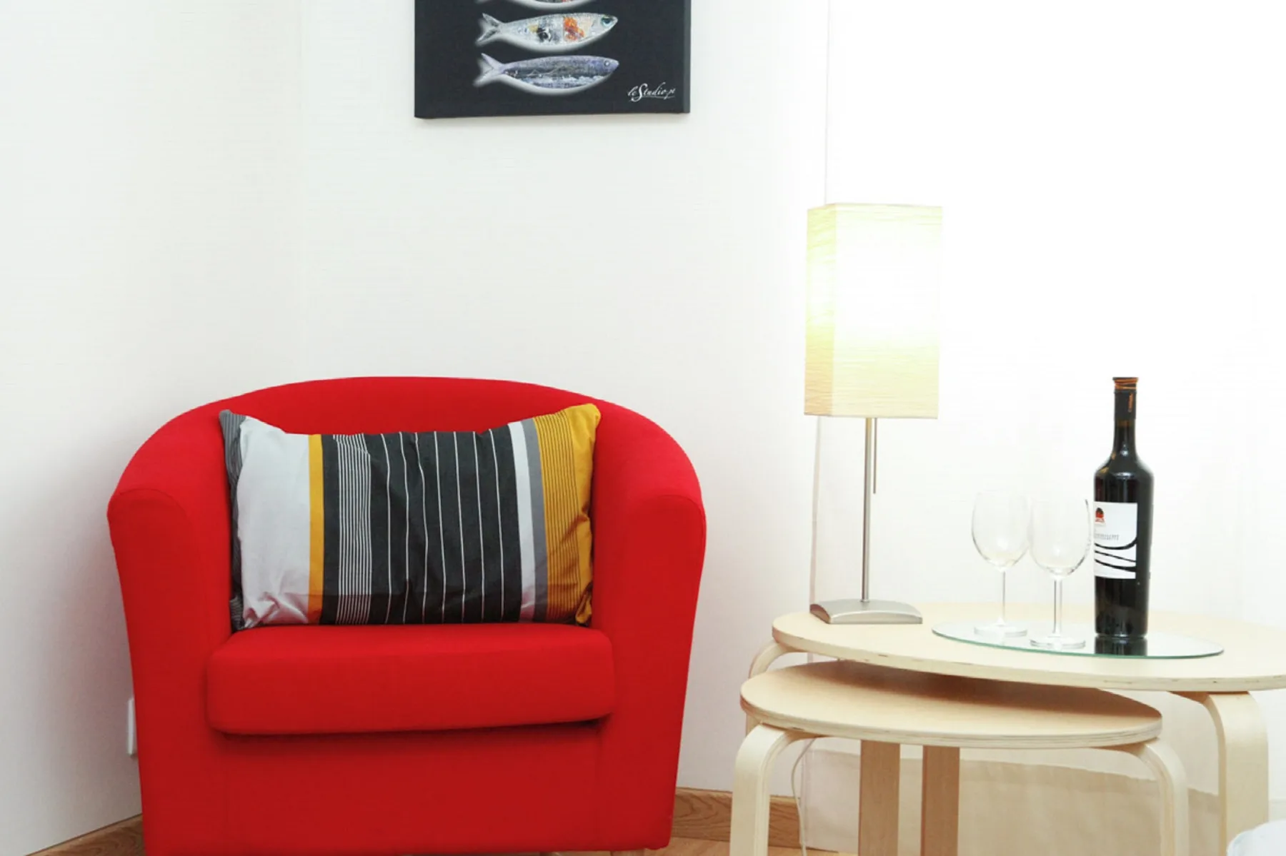 A bright sitting area features a red armchair beside a small table and lamp.
