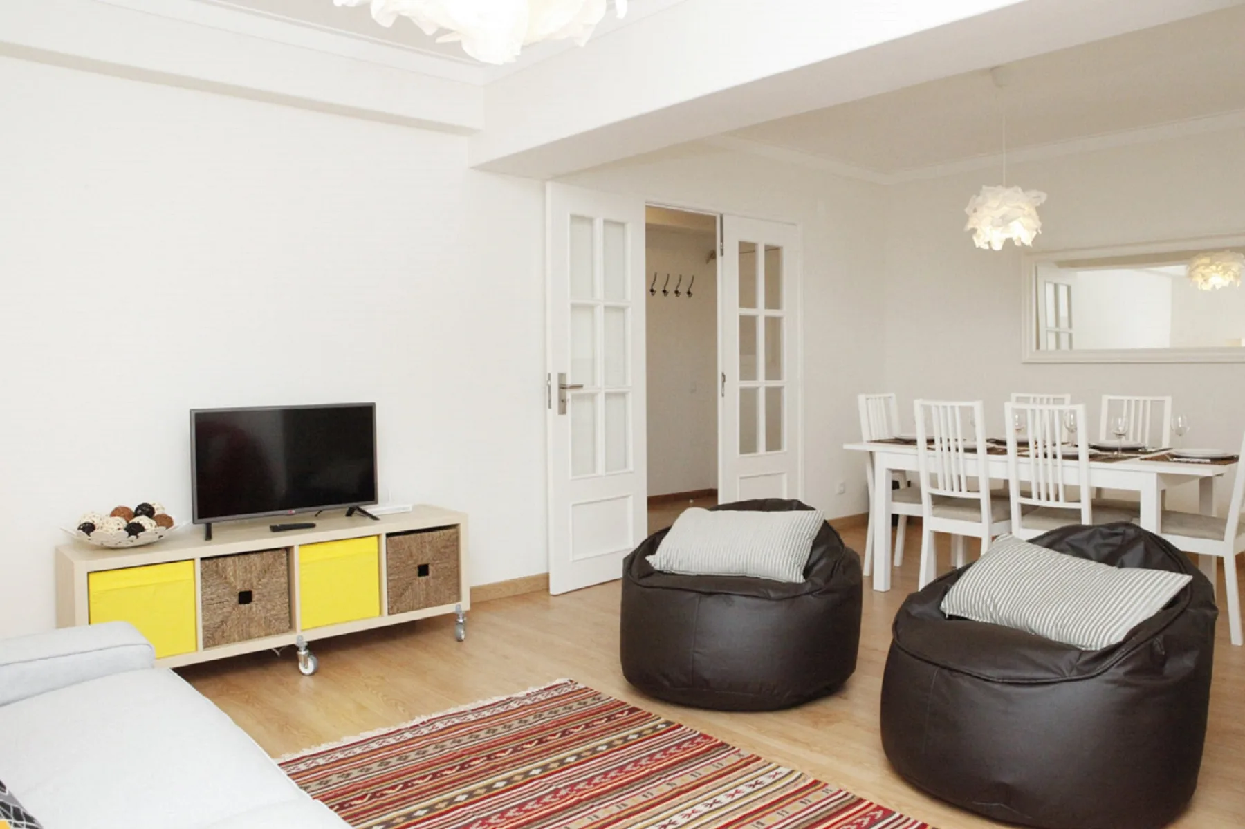 A bright living and dining area with a television, table, and floor cushions.