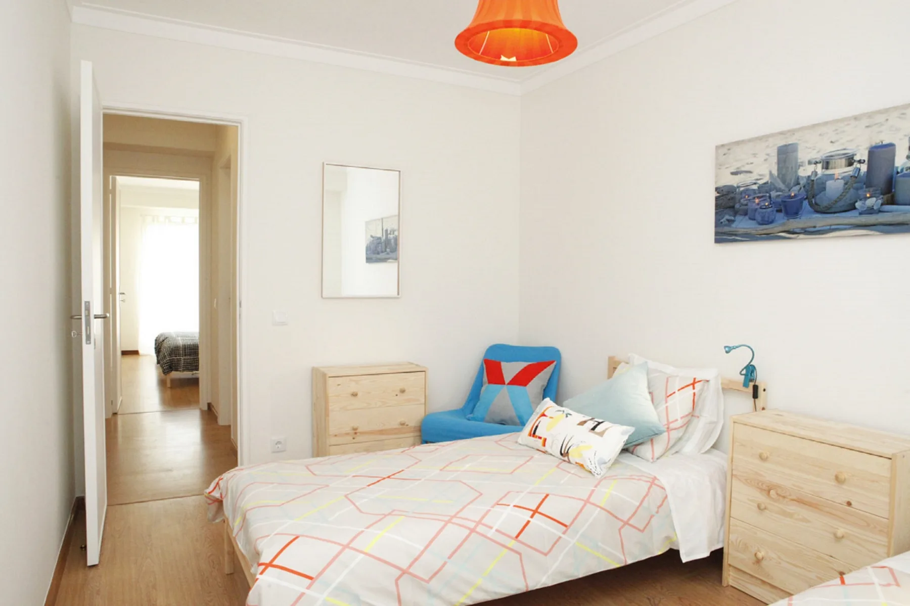 A bright bedroom with a neatly made bed and colorful geometric bedding.