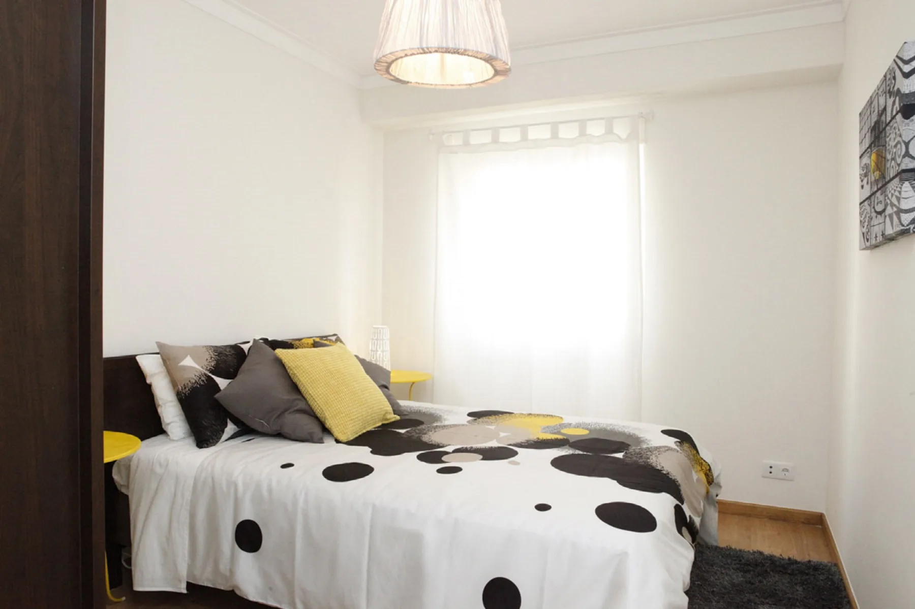 A bright bedroom with a bed covered in a black-and-white patterned duvet.