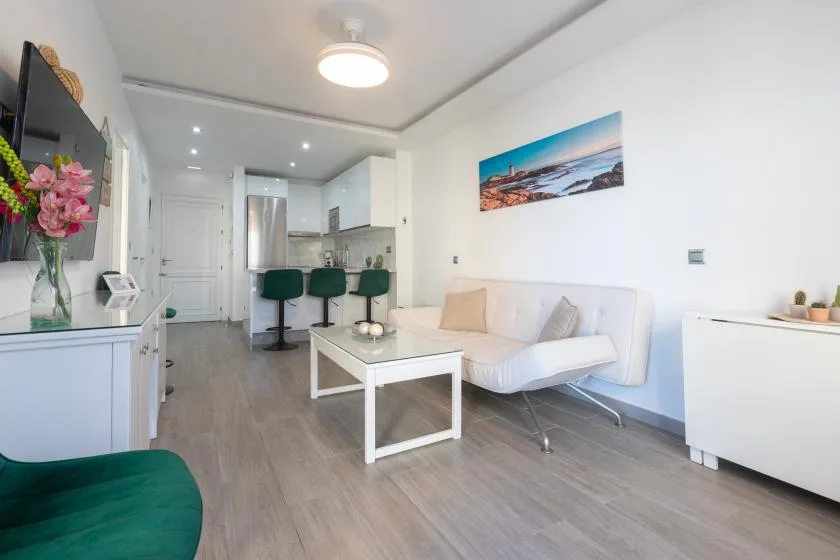 A bright living room with seating, a coffee table, and a compact kitchen area.