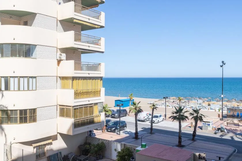 A seaside apartment building overlooks a beach with rows of umbrellas.