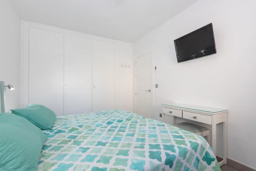 A bedroom with a bed covered in a turquoise and white patterned quilt.