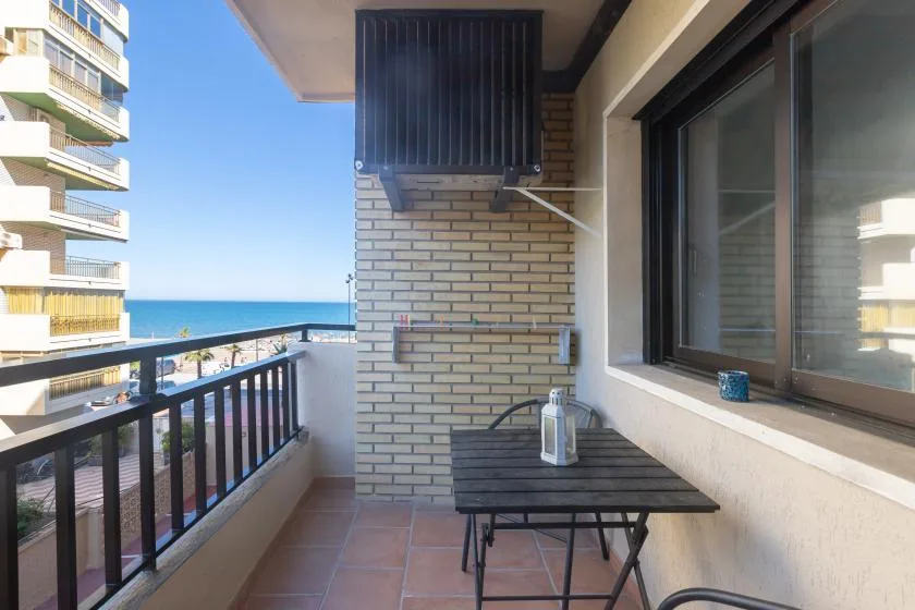 A balcony with a small table and seating overlooks the sea.