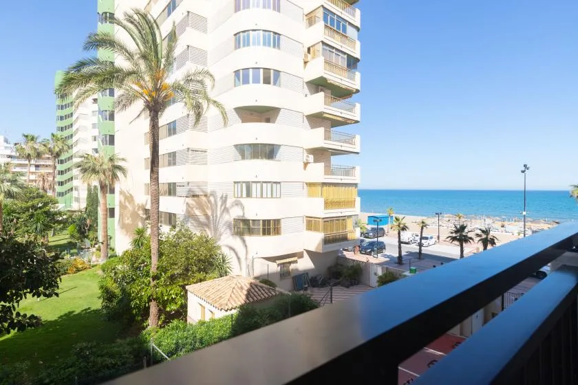 A balcony overlooks a curved white building, palm trees, and the beach.