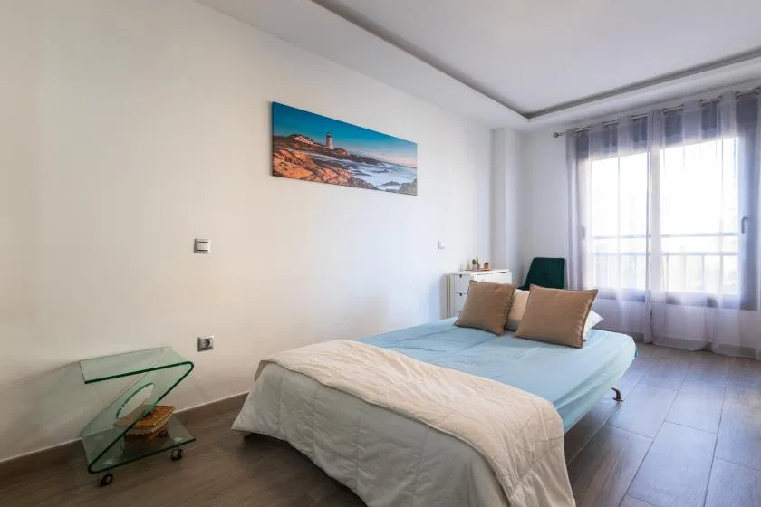 A bedroom with a neatly made bed beside a large window.