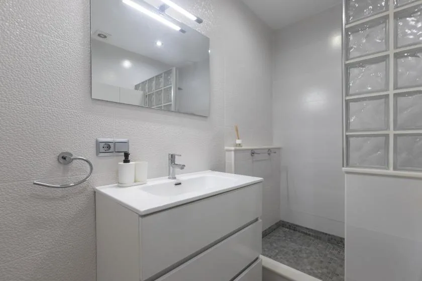 A bright bathroom with a white sink, wall mirror, and glass-block window.