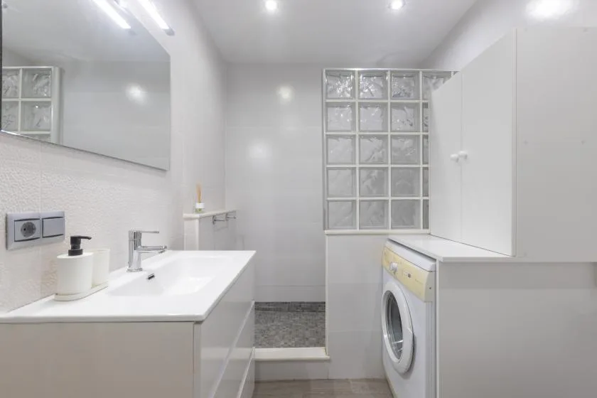 A bright bathroom with a sink, washing machine, and glass-block window.