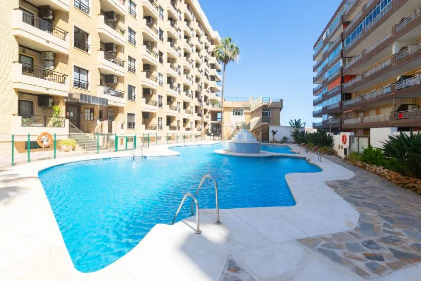 A swimming pool sits between apartment buildings under a clear blue sky.
