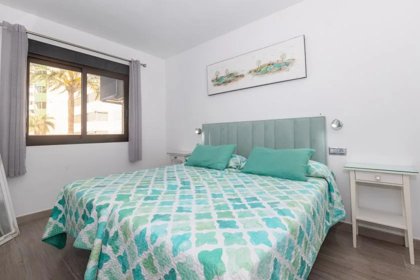 A bedroom with a bed covered in a turquoise and white patterned bedspread.