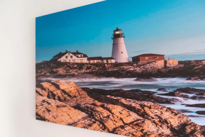 A framed coastal scene shows a lighthouse above rocky shoreline and waves.