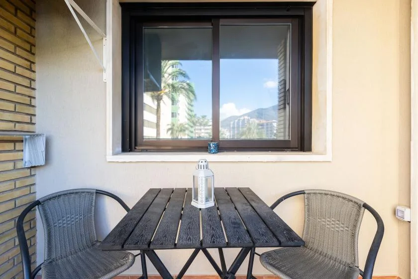 A small outdoor dining area with a dark table and two chairs beside a window.