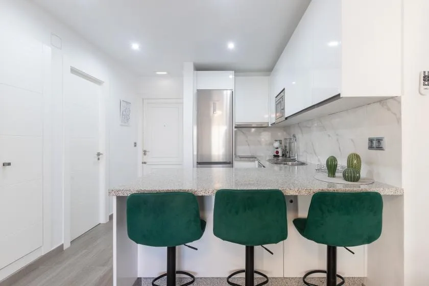 A bright kitchen with a counter, green seating, and white cabinets.