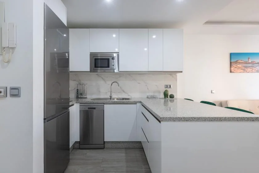 A modern kitchen with white cabinets, stainless steel appliances, and a long counter.