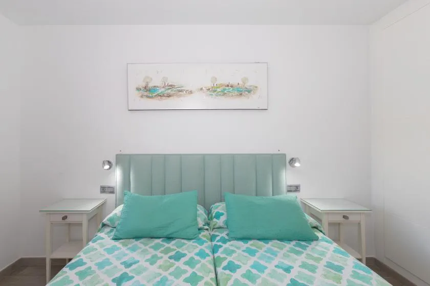 A bedroom with a bed dressed in turquoise and white bedding beneath framed artwork.