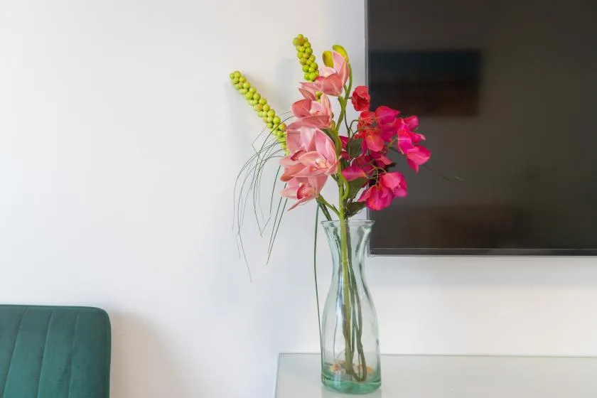 A colorful flower arrangement sits in a glass vase beside a wall-mounted screen.