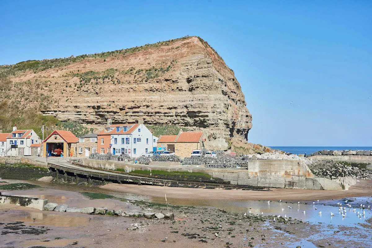 A coastal village sits beside a large layered rock cliff and shallow tidal water.
