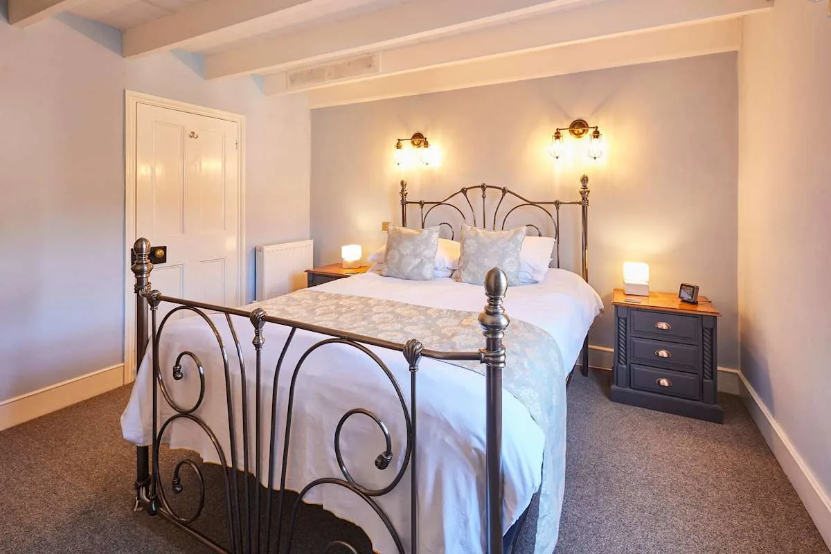 A bedroom with a bed, bedside tables, and wall lights.