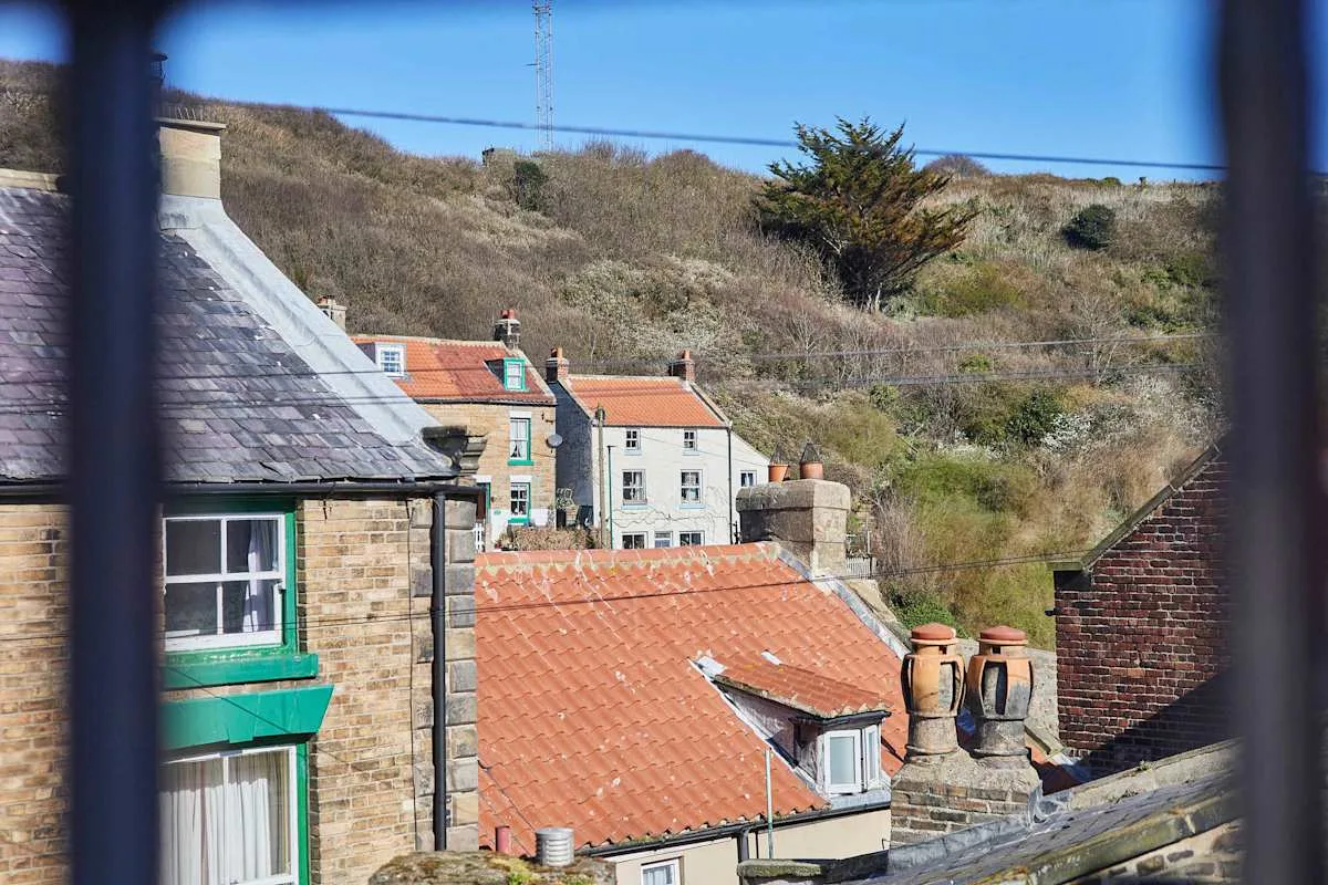 Rooftops and hillside buildings viewed through a railing under a clear sky.