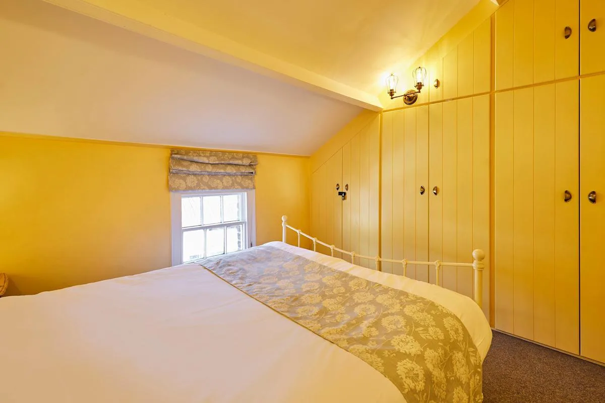 A bedroom with a bed, yellow built-in cabinets, and a window.