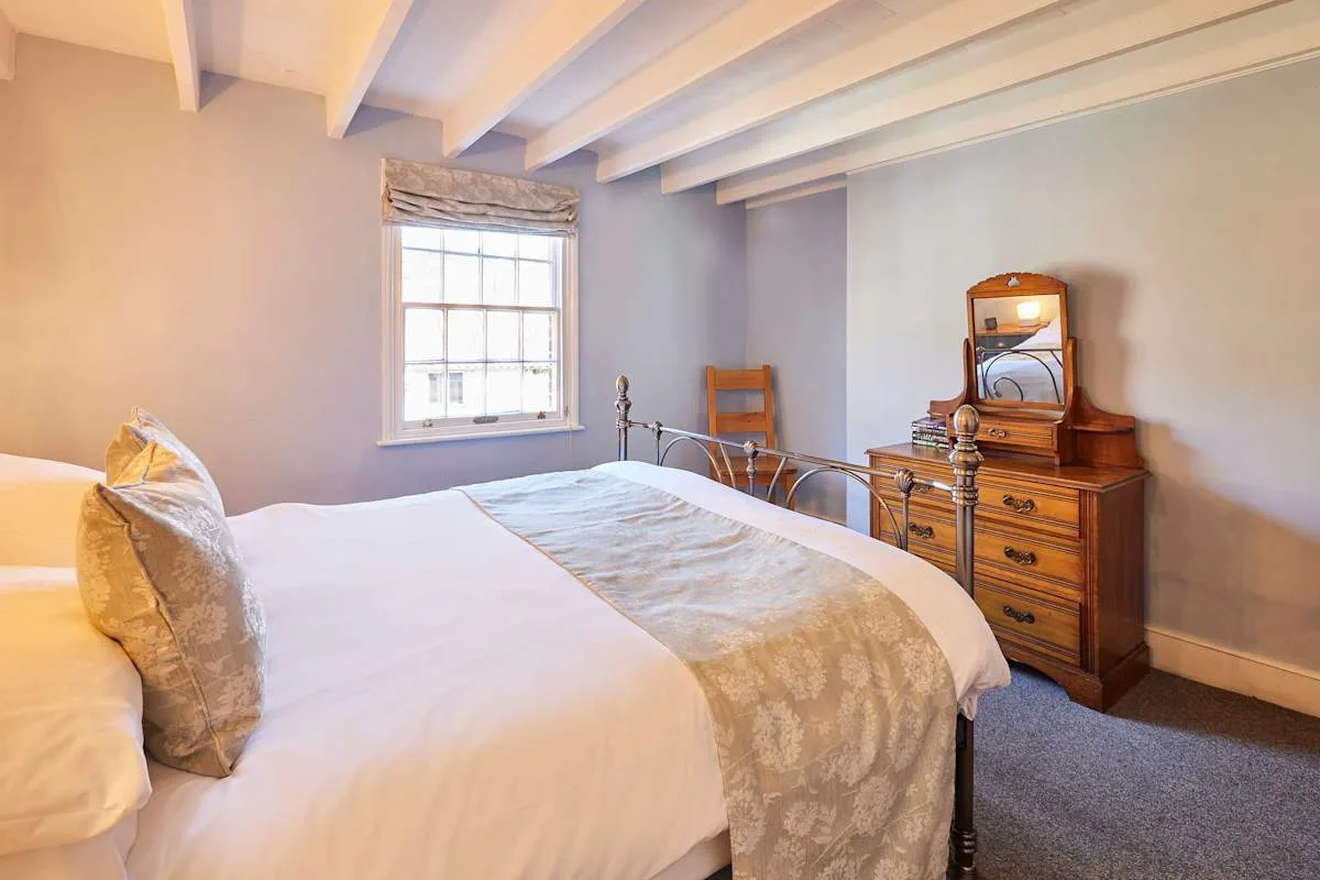A bedroom with a bed beside a window and wooden dresser.