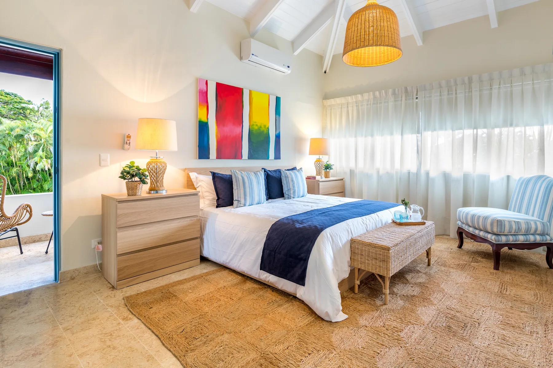 Un dormitorio luminoso con una cama, mesitas de noche y una gran ventana con cortinas.
