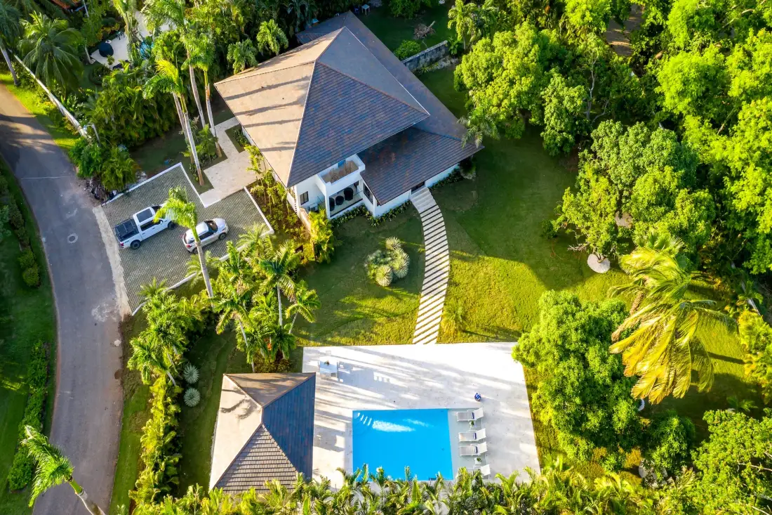 Vista aérea de una casa, césped y piscina rodeados de abundante vegetación.